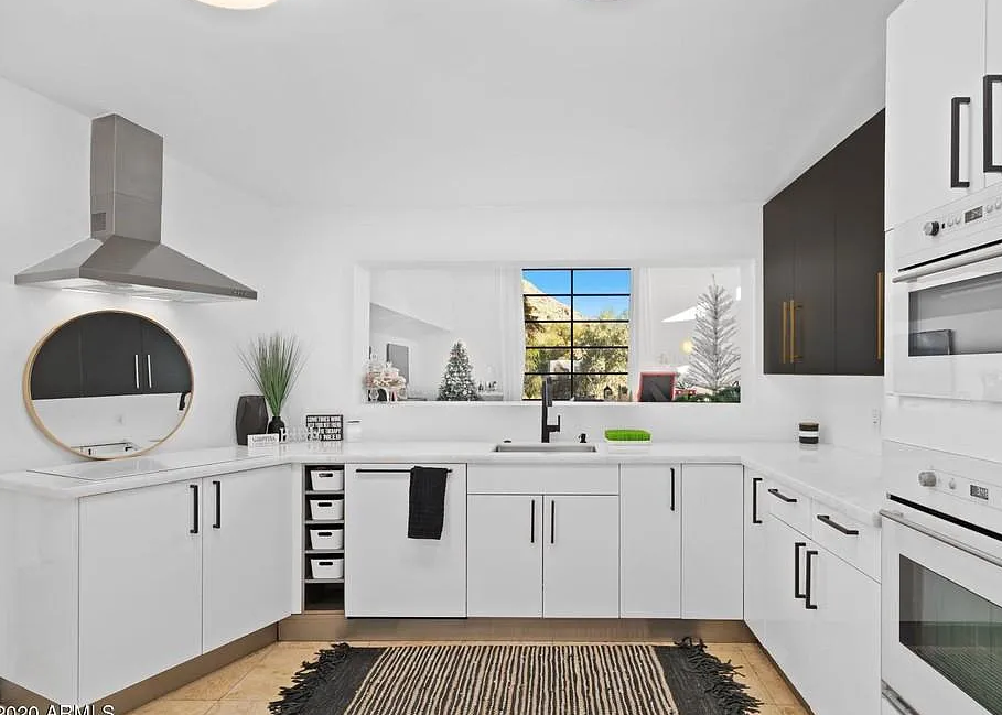Modern white kitchen with black hardware, range hood, mountain window view and double oven